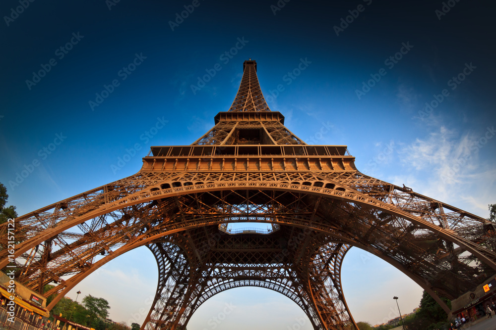 Wall mural a low angle fisheye shot of the eiffel tower in paris, france, against a clean blue sky