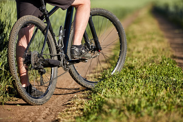 Fototapeta premium Closeup of cyclist man legs with mountain bike on outdoor trail in the summer field.