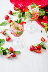 Alcoholic and non-alcoholic refreshing drinks, cold sparkling cocktail with ice, green mint and fresh strawberries in a beautiful glass on a light background 