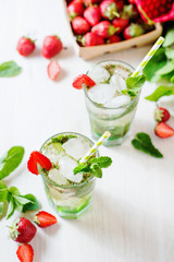 Alcoholic and non-alcoholic refreshing drinks, cold sparkling cocktail with ice, green mint and fresh strawberries in a beautiful glass on a light background 