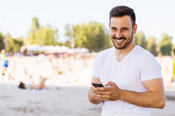 Young man typing on mobile phone against a beach background