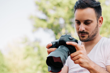 Handsome young man holding a DSLR camera with image check.