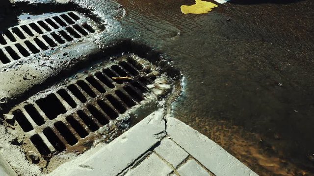 Rainwater flows on the asphalt road and fall into the metal hatch with holes drain.