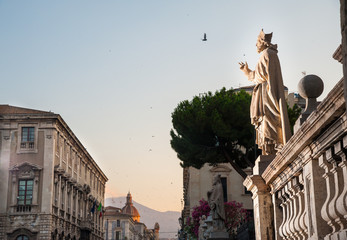 Fototapeta premium Statue outside the Church of St. Agatha in Catania, Sicily, with the town and Mount Etna in the background