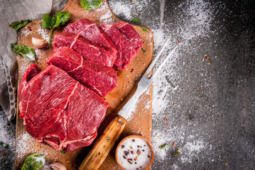 Meat. Beef, veal. Fresh raw tenderloin, piece without bone. For frying grilling barbecue. Cut into steaks, whole. On black stone table,cutting board, spices, salt, fork for meat. Top view copy space