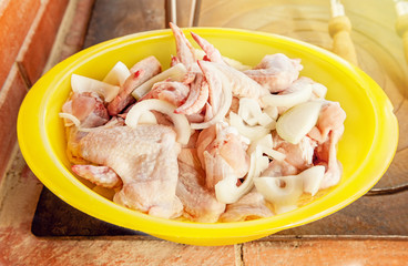 Chicken wings prepared for frying, grilling, laying in a big yellow bowl on the stove. The horizontal frame.