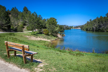 Fototapeta na wymiar a view of blue Lac de Cavayere , artificial lake near Carcassone with green vegetation and a bench