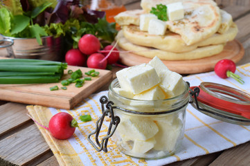 Square cubes of traditional greek cheese feta with flat bread, lettuce, onion and radish on wooden background.