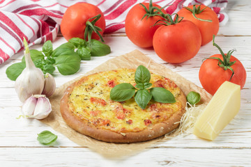 Baked flat bread with tomatoes, cheese, garlic and Basil on a white wooden table. Rustic style. Selective focus