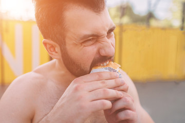 Man eats a hamburger after a workout. Very hungry, fatty and unhealthy food