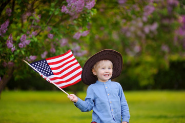 Cute toddler boy holding american flag in beautiful park