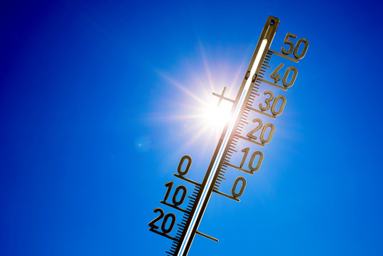 Thermometer mit strahlender Sonne und blauem Himmel im Hintergrund
