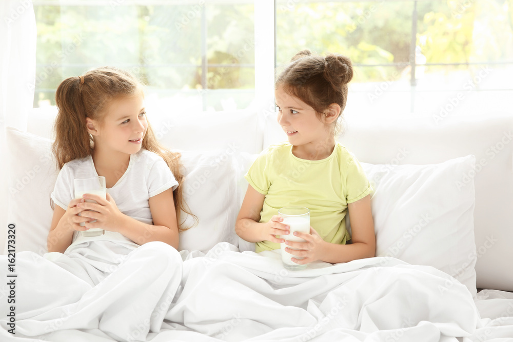 Poster Portrait of two little girls in bed with glasses of milk