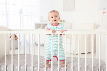 Cute little baby standing in crib at home