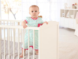 Cute little baby standing in crib at home