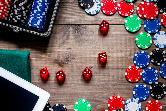 Compulsive gambling. Poker chips and the dice nearby tablet on wooden table top view copyspace