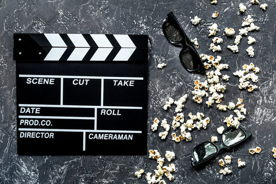 Watching the film. Movie clapperboard, sunglasses and popcorn on grey stone table background top view