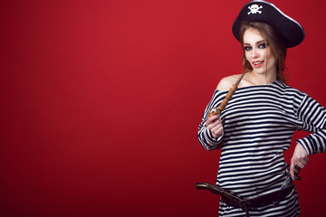 Portrait of gorgeous woman with provocative make-up wearing pirate costume and cocked hat holding a wooden carved tobacco pipe, a gun and dagger in her belt. Copy space