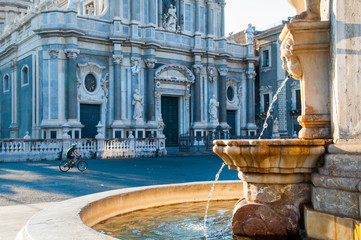 View of the fountain at the basis of famous lava stone elephant in the main square of Catania, Sicily, with a view of St. Agatha church