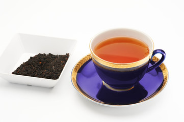 Cup of black tea and little bowl with tea leaves