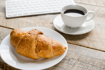 Businessman morning with keyboard, cup of coffee and croissant on wooden table background