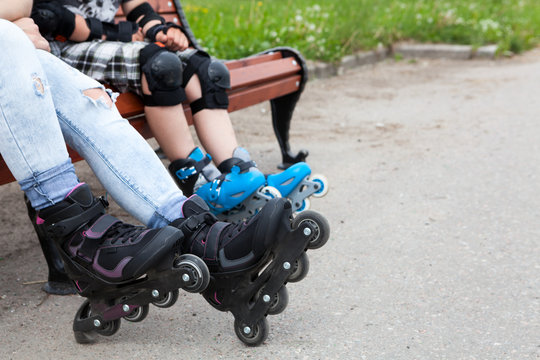 Close up view at the roller-skates wearing on female and boy legs, people sitting on the bench