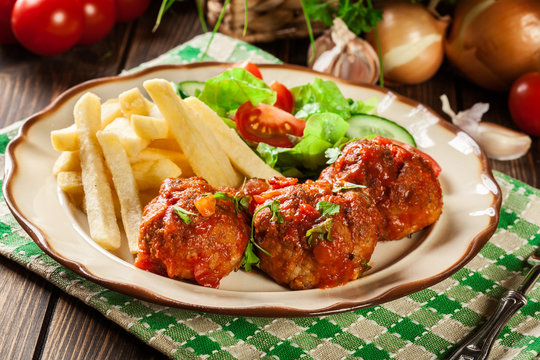 Roasted meatballs in tomato sauce with french fries and salad