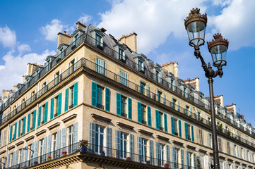 Fototapeta na wymiar A typical Haussmannian building in Paris with balconies and shutters and a street light in the foreground under a warm light of late afternoon.