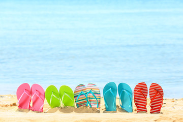 Naklejka premium Colorful flip-flops on sand at sea shore. Vacation concept