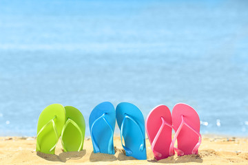 Fototapeta premium Colorful flip-flops on sand at sea shore. Vacation concept
