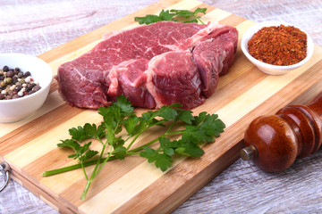 Raw beef steak with spices Leaves of coriander on wooden cutting board. Ready for cooking.
