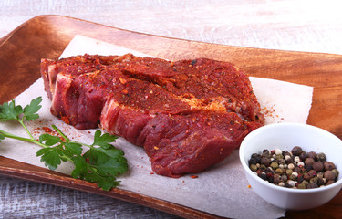 Raw beef steak with spices Leaves of coriander on wooden cutting board. Ready for cooking.