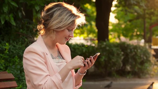 Attractive white woman blonde using a smartphone in park at sunny day