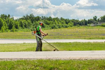 A lawn-mower with trimmer mowing grass along road. Side view