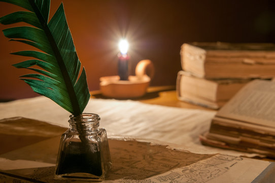 Quill pen, old papers and books by candle light