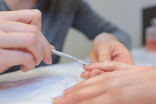 close up of professional manicurist using cuticle pusher doing manicure
