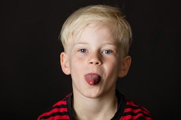 Playful little blond boy sticking out his tongue