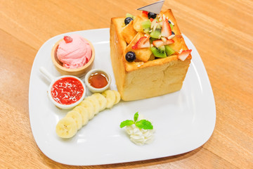 Honey Toast. Bread buttered toast. Topped with honey, banana and fruit decorations. A side of whipped cream, ice cream. Top view
