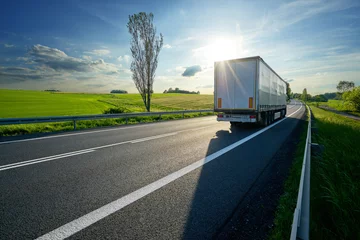 Foto op Aluminium Vrachtwagen rijden op asfaltweg langs de groene velden in het landelijke landschap bij zonsondergang © am