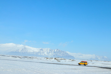 A yellow mini van is travelling on the raod with mountain as the background in Iceland