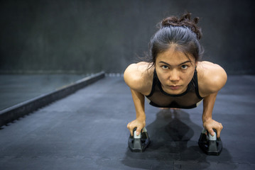 Fototapeta na wymiar Young Asian athlete woman doing push up with push-up bars on the floor, sport and training in fitness gym concepts
