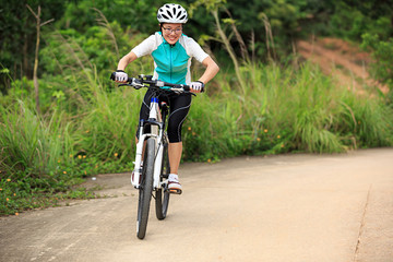 woman cyclist cycling on summer forest trail