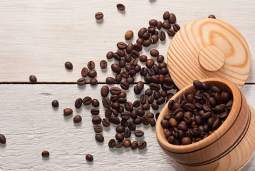 Coffee beans scattered from a Cup on white wooden background, wooden utensils,