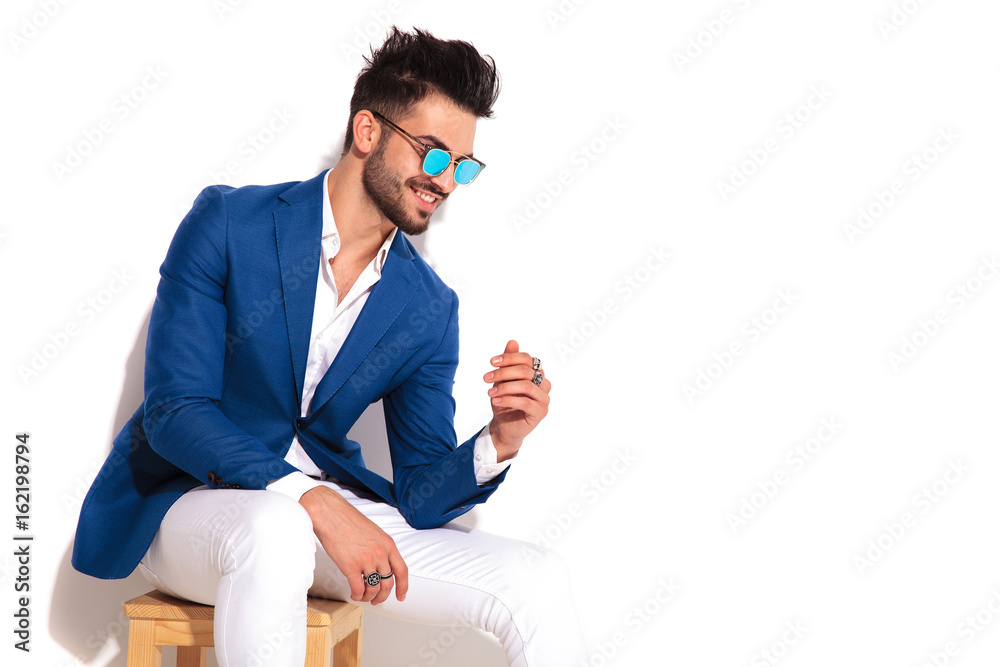 Poster side view of laughing elegant young man sitting on chair