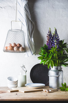 Concept of rural kitchen. Lupines in a can, milk, eggs and ware on a wooden table against the background of a white wall