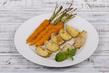 Young potatoes, carrots, onions, peppers, garlic baked in the oven on the white plate