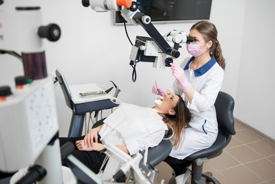 Female dentist with dental tools - microscope, mirror and probe checking up patient teeth at dental clinic office. Medicine, dentistry and health care concept. Dental equipment
