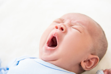 Sleepy adorable newborn baby yawning in bed