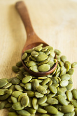 Raw pumpkin seeds in a wooden spoon on a light wooden background. Selective focus. Close-up. Vertical.