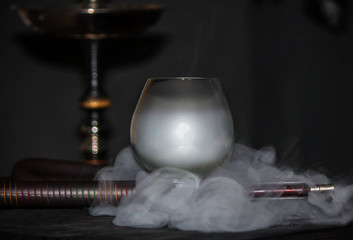 Heavy hookah smoke under a brandy glass on a gray background, hookah tube